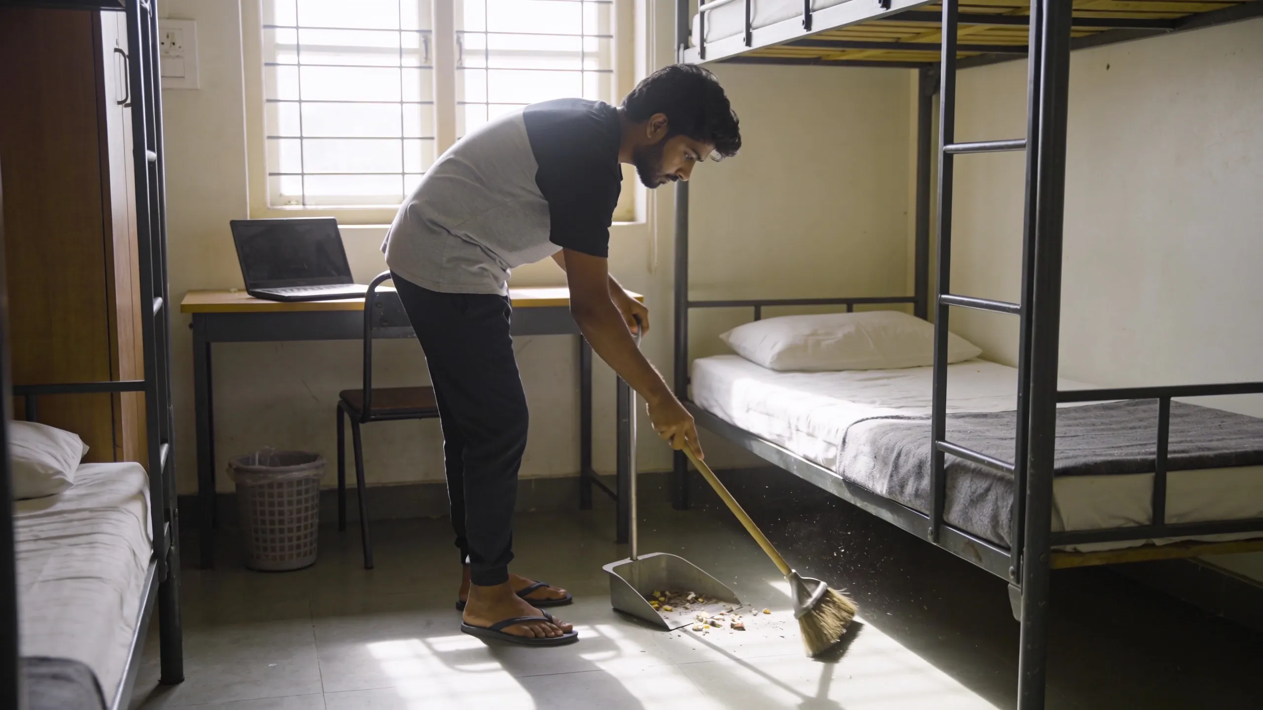 Student sweeping hostel room floor with broom during weekly cleaning routine India